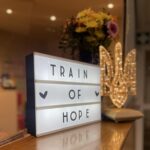 Blumen, Letterbox mit Schriftzug "Train of Hope" und ein leuchtendes ukrainisches Wappen